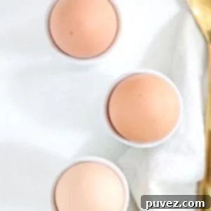 Three brown hard-boiled eggs in white egg cups.