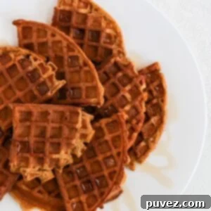 Cozy Autumn Whole Wheat Pumpkin Waffles Recipe 5 Quarters of round pumpkin waffles overlapping and topped with a drizzle of maple syrup on a white plate.