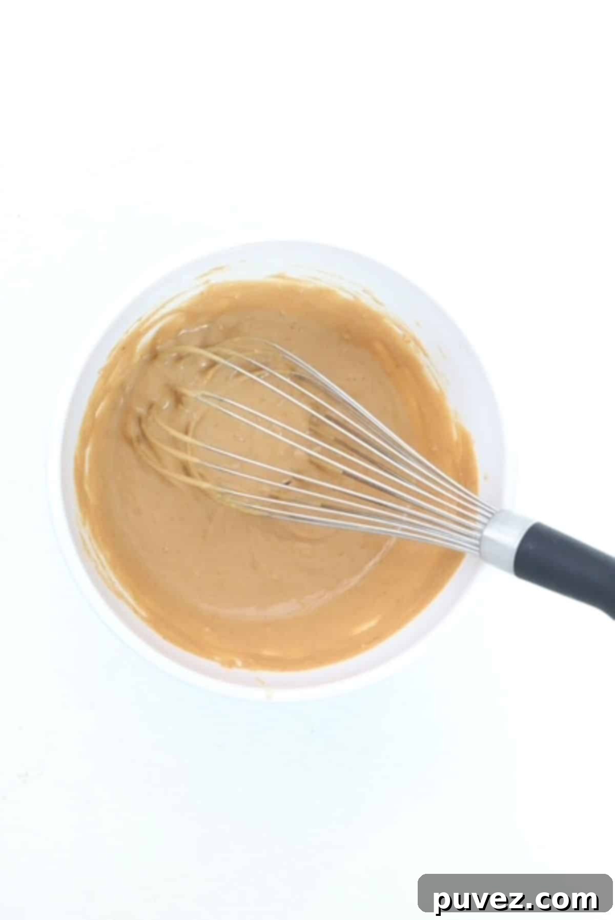 Peanut butter sauce in a white bowl with a whisk.