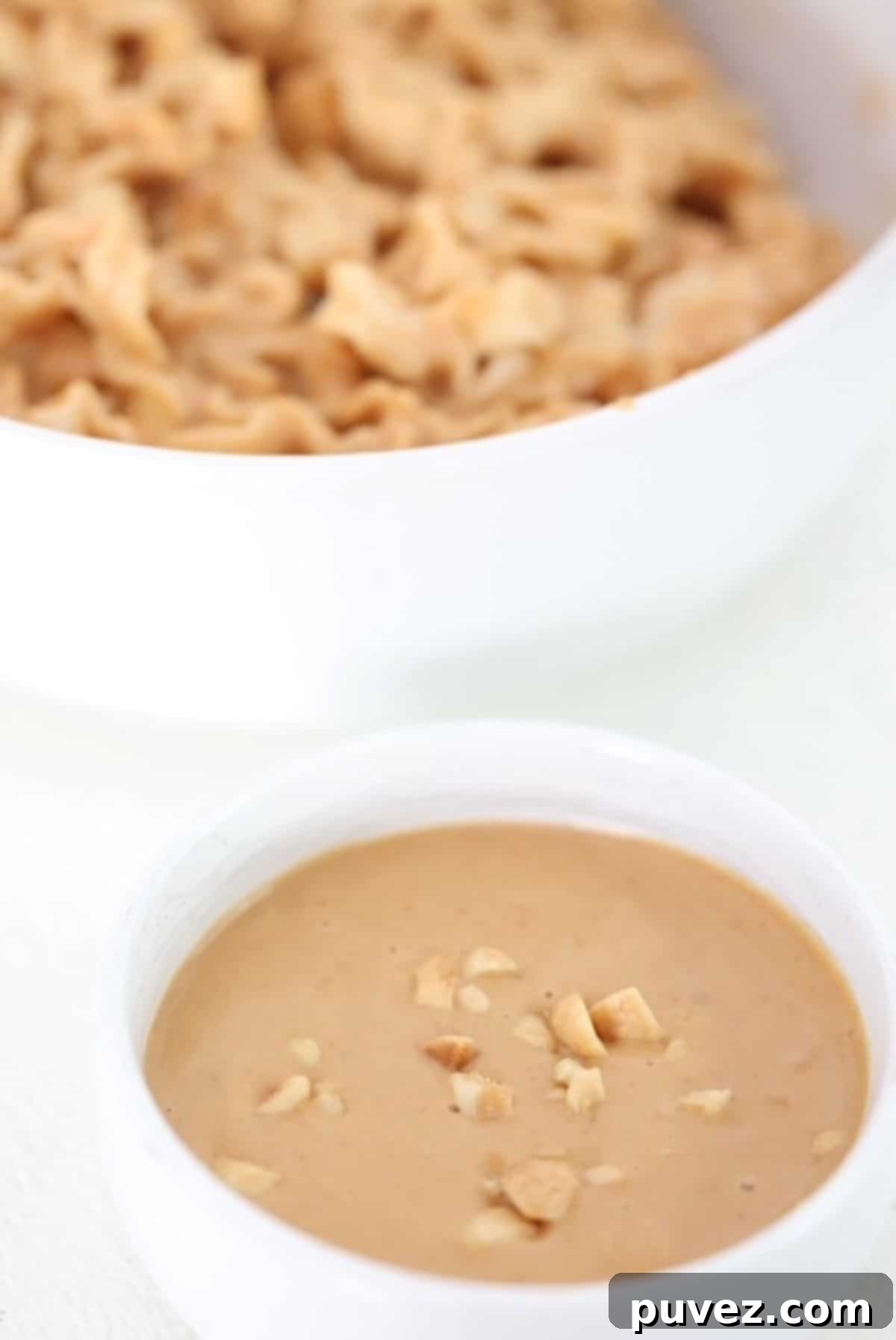 A small bowl of peanut butter sauce with a bowl of peanut butter noodles behind it.