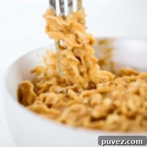 A bowl of noodles in a peanut butter sauce with some wrapped around the prongs of a fork.