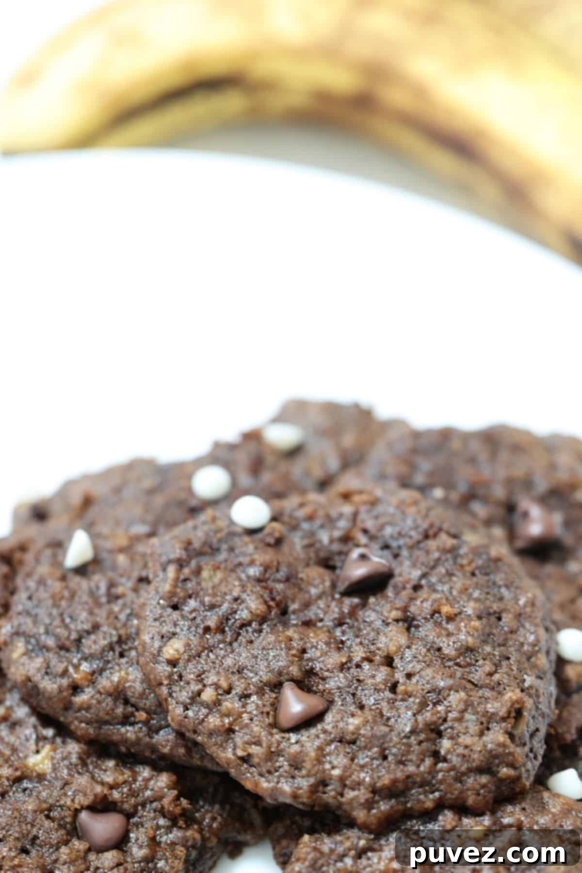 Banana Cocoa Cookies on a white plate with overripe bananas in the background, showcasing their delicious texture.