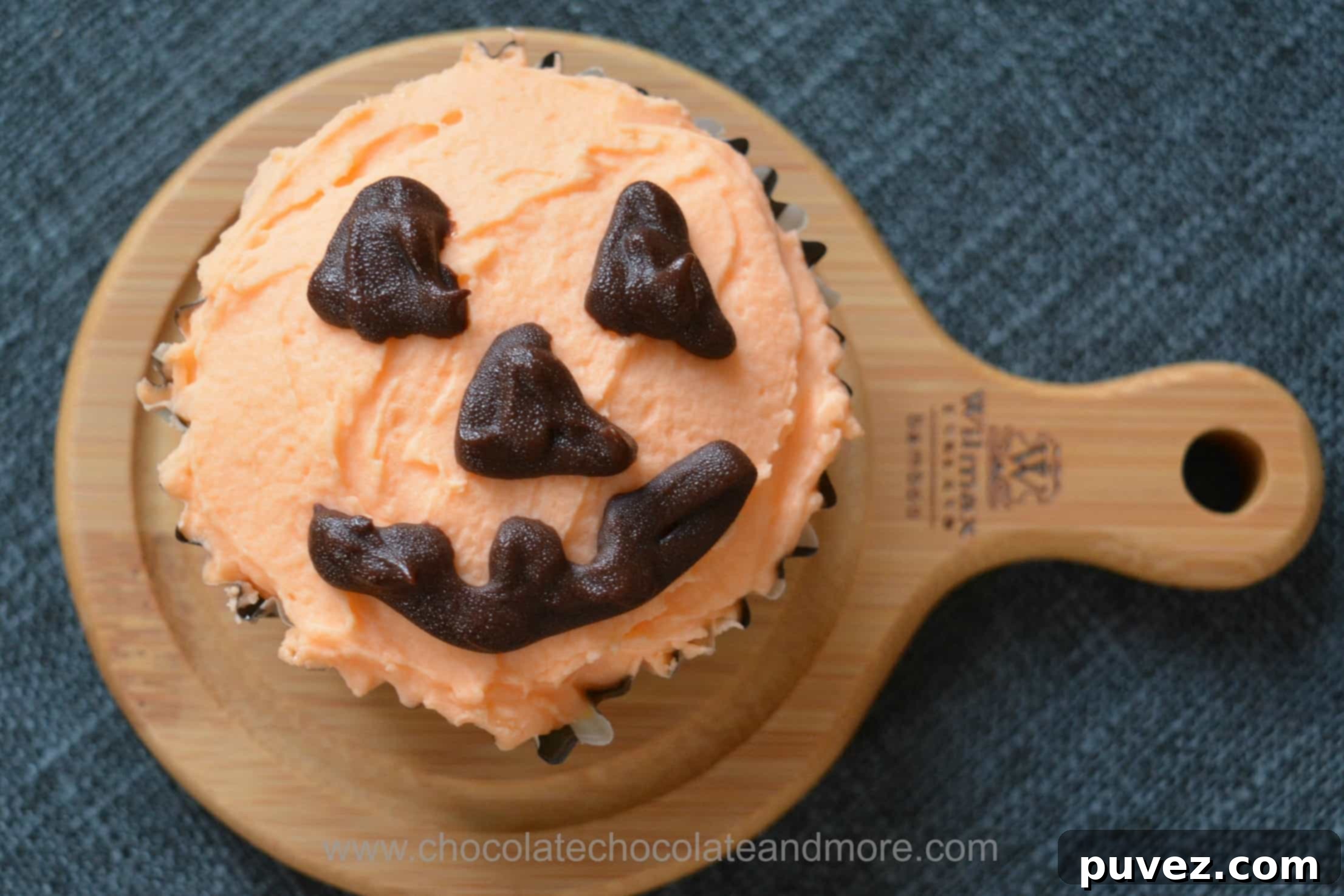 A delicious yellow cupcake decorated with orange frosting and a pumpkin face for Halloween