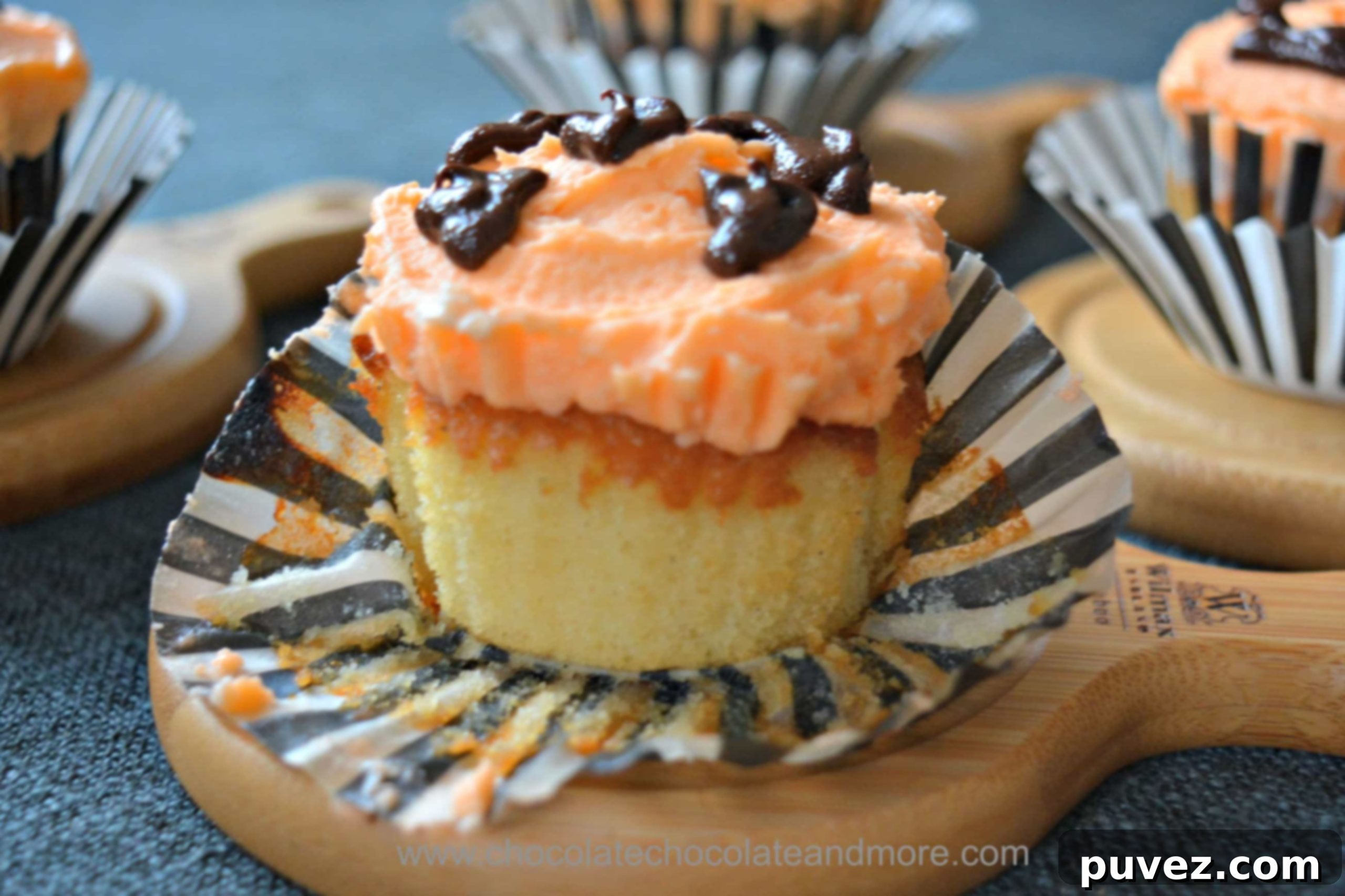 Three yellow cupcakes, one with orange frosting and a pumpkin face, another with chocolate frosting and sprinkles, and a third plain