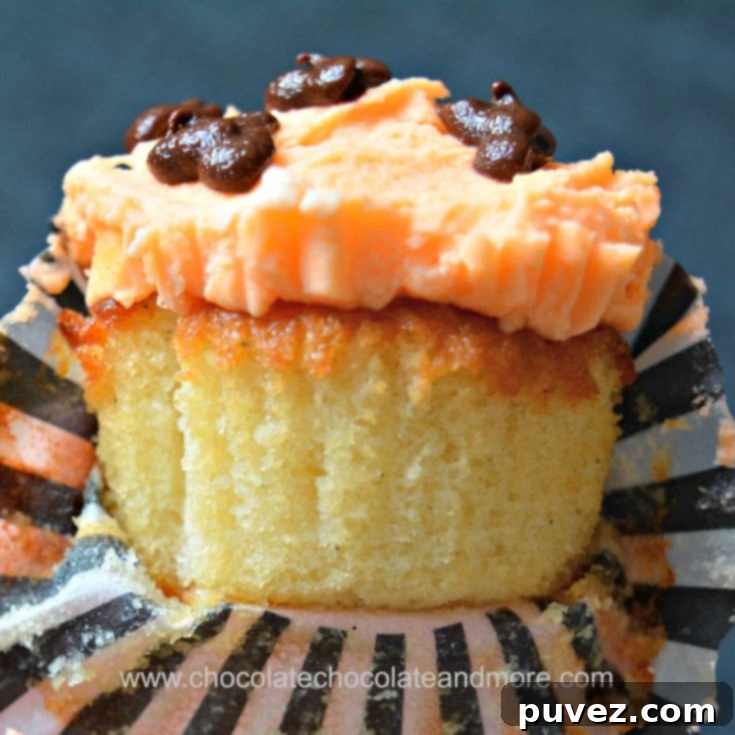 A delicious yellow cupcake with orange buttercream frosting and a pumpkin face.