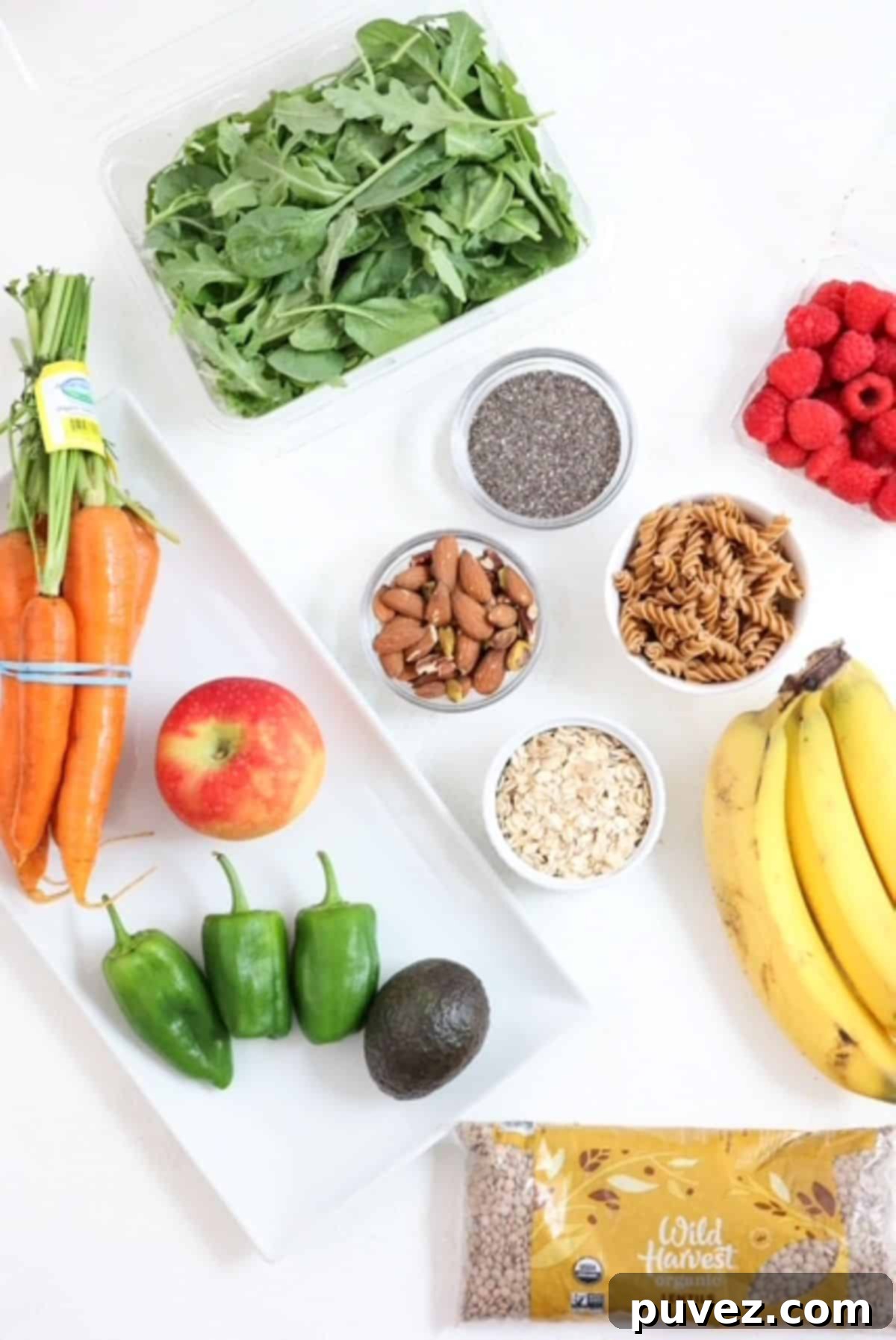 A vibrant top-down view of a variety of high-fiber foods including fresh fruits, colorful vegetables, an assortment of nuts and seeds, and various whole grains, beautifully arranged on a clean white board, highlighting options for a fiber-rich diet.