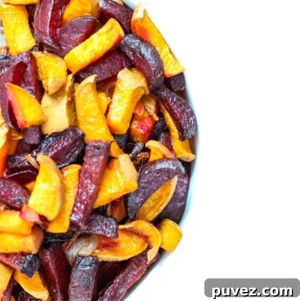 Roasted beets and sweet potatoes in a white bowl, garnished with fresh herbs.
