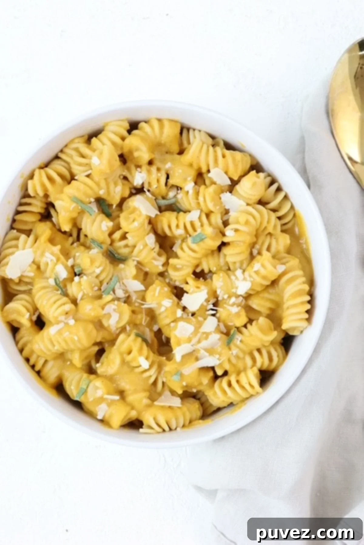 Pasta with butternut squash sauce in a white bowl topped with parmesan cheese and fresh sage.