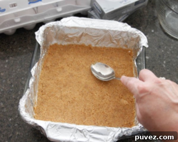 A perfectly pressed graham cracker crust base for Classic Cheesecake Bars in an 8x8 baking pan.