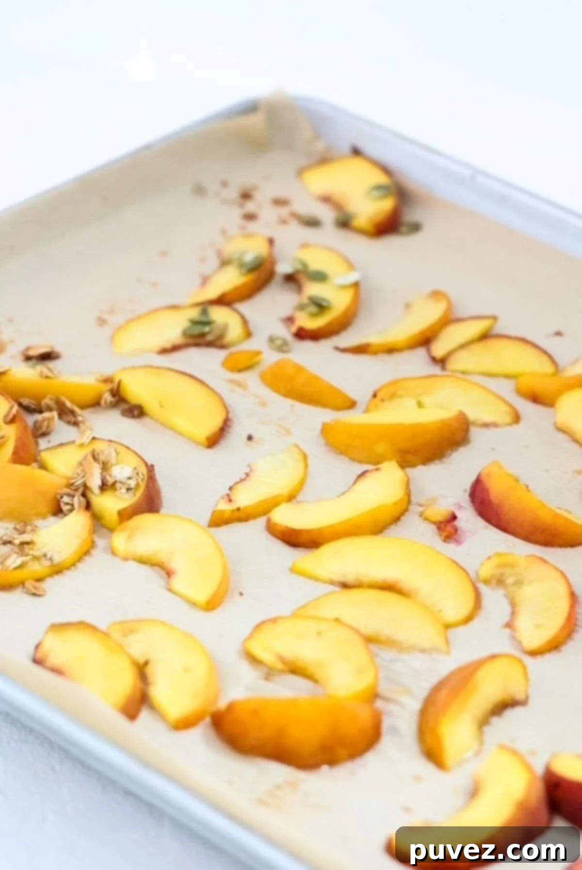 Sliced roasted peaches on a lined baking sheet, golden and caramelized at the edges.