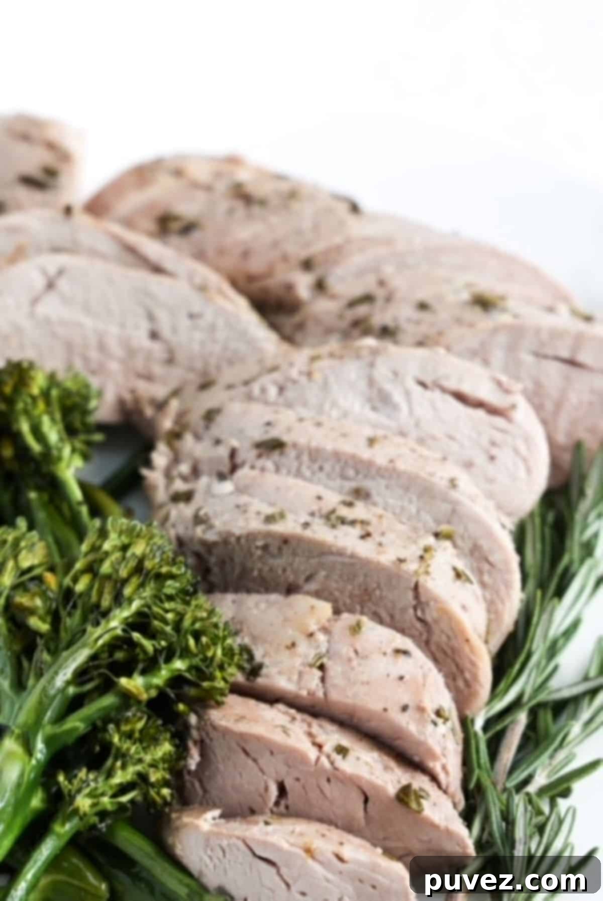 Sliced pork tenderloin with broccolini to the left and a sprig of fresh rosemary to the right.