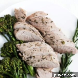 Slices of roasted pork tenderloin with broccolini to the left and fresh rosemary to the right of the cooked tenderloin.