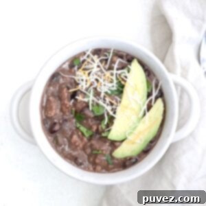 Top view of a bowl of chili with ground turkey and black beans topped with two slices of avocado and a sprinkle of cheese.